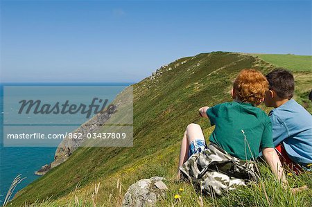 UK,Wales,Pembrokeshire. Two boys sit looking out over Fishguard Bay and the Irish Sea from the Pembrokeshire Coastal Path on Dinas Head.