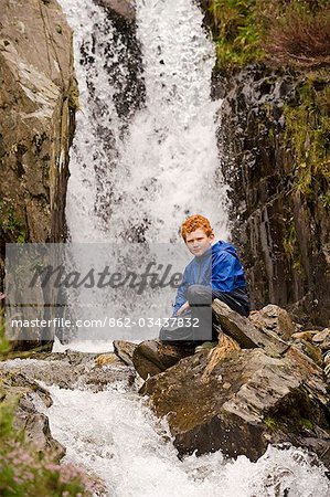 Wales, Conwy, Snowdonia. Ein kleiner Junge sitzt neben einem Wasserfall in Cwm Idwal am Fuße des die Glyders