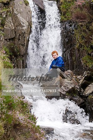 Wales, Conwy, Snowdonia. Ein kleiner Junge sitzt neben einem Wasserfall in Cwm Idwal am Fuße des die Glyders