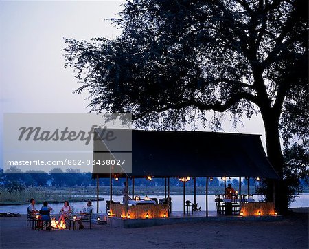 Assis autour du feu de camp à côté de la grande tente salle à manger qui donne sur le fleuve Zambèze, Old Mondoro bushcamp. Assis autour du feu de camp à côté de la grande tente salle à manger qui donne sur le fleuve Zambèze, Old Mondoro bushcamp.