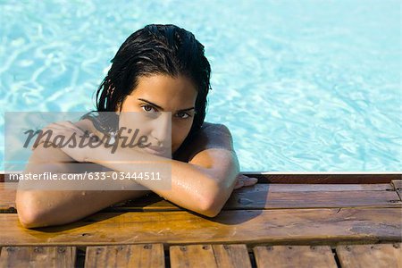 Woman in water resting at edge of swimming pool, portrait