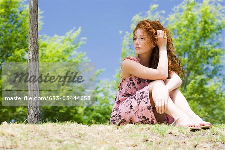 Young woman sitting outdoors, looking away in thought
