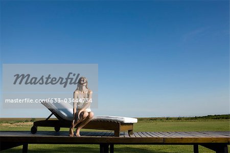 Woman sitting on lounge chair outdoors, looking up dreamily