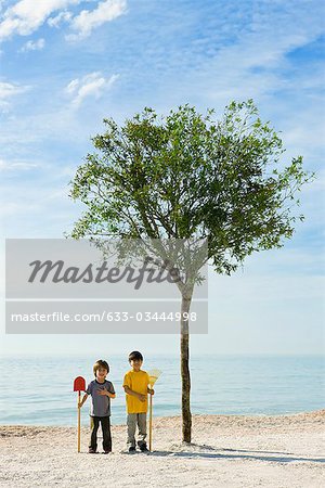 Ökologie, ConceZS, Jungs mit Gartengeräten stehend von Baum wächst am Strand