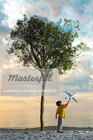 Garçon jouant avec le jouet avion sous les arbres sur la plage