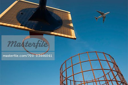 Basketball Hoop, an Empty Gasometer and Jet Plane Against Blue Sky