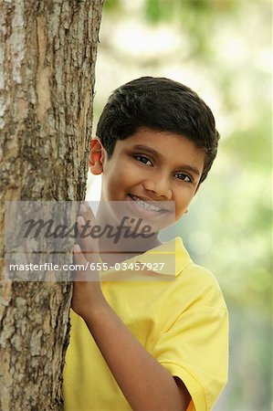 Young boy peeking out from behind a tree