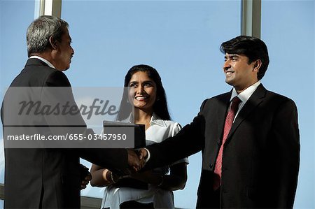 Business men shaking hands while female colleague looks on.