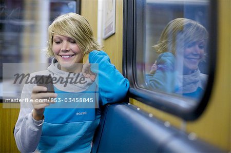 Young woman using mobile phone in city train, front view