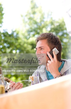 Young man talking on mobile phone and eating, low angle view