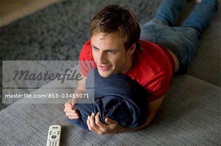 Junger Mann liegend auf der Couch, mit einen Kissen, erhöht, Ansicht