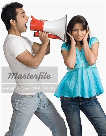 Side profile of a young man blowing a bullhorn with a teenage girl covering her ears
