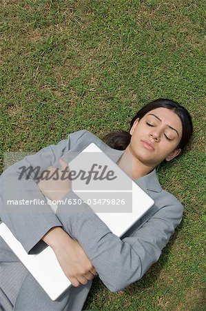 Businesswoman lying on grass and hugging a laptop