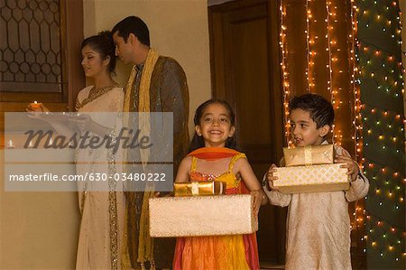 Children holding gifts with their parents holding religious offering in the background