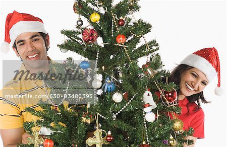Portrait of a couple peeking through a Christmas tree