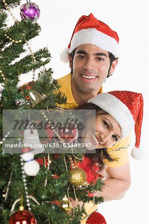 Portrait d'un couple furtivement à travers un arbre de Noël et souriant