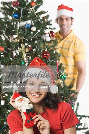 Femme montrant un bas de Noël avec un homme décorer un arbre de Noël dans l'arrière-plan