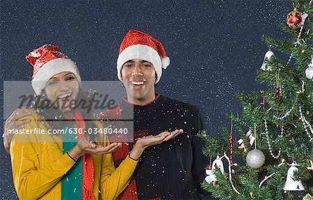 Couple standing in snow near a Christmas tree and smiling