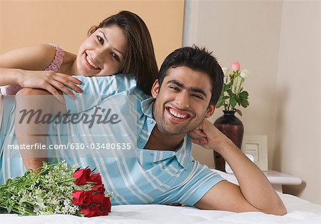 Portrait of a couple lying on the bed with bouquet of flowers