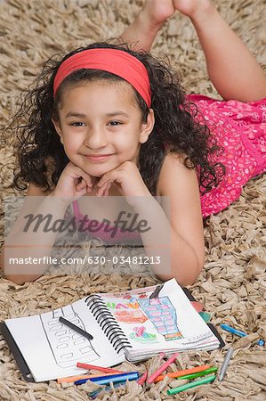 Girl lying with a notebook and colored pencils