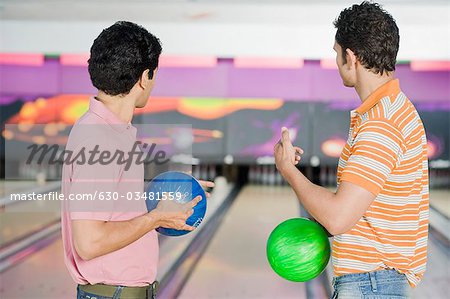 Deux jeunes hommes tenant des boules dans un bowling