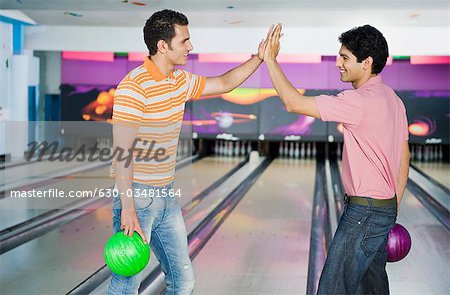 Deux jeunes hommes High-Five dans une ruelle de bowling