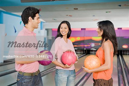 Young couple with their friend holding bowling balls in a bowling alley