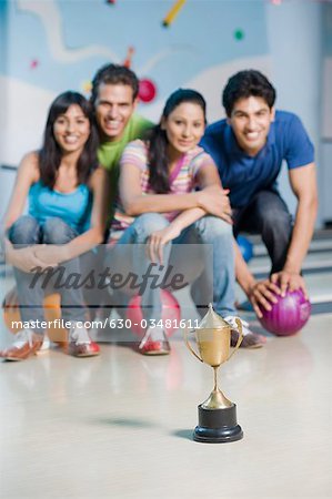Deux jeunes couples avec des boules de bowling et un trophée dans une allée de quilles