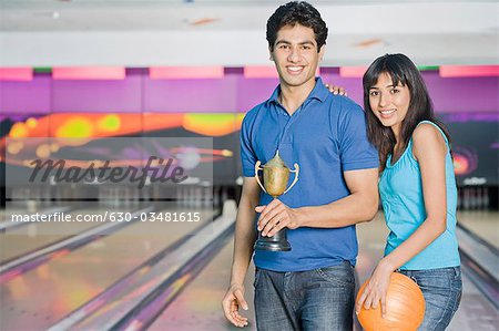 Jeune couple avec une boule de bowling et un trophée dans un bowling