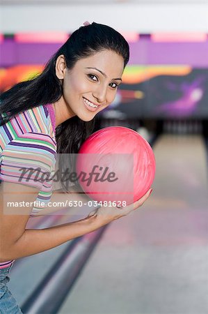 Jeune femme tenant une boule de bowling dans une allée de quilles