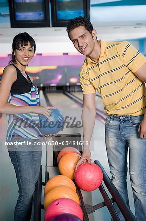 Young couple picking bowling balls and smiling in a bowling alley