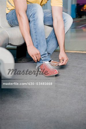 Low section view of a young man tying his shoelace in a bowling alley