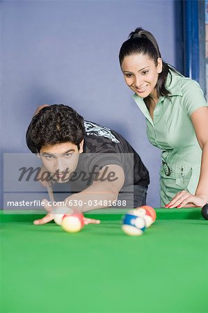 Young man playing pool and a young woman watching his game