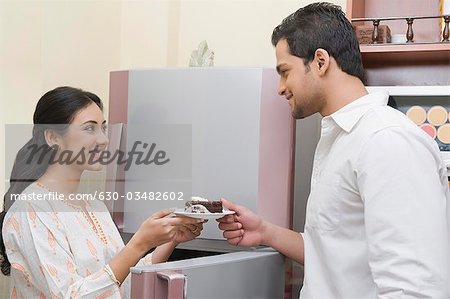 Femme donnant une assiette de gâteau à un homme devant un réfrigérateur