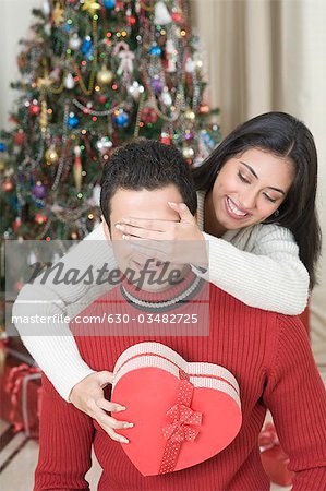 Woman covering her husband's eyes before giving a surprise gift