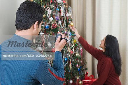 Man filming his wife decorating Christmas tree