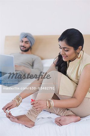 Woman painting toenails while her husband working on a laptop