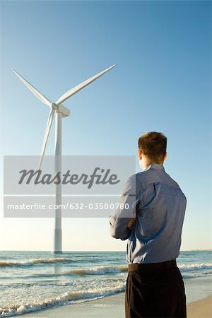 Businessman on beach looking at offshore wind turbine