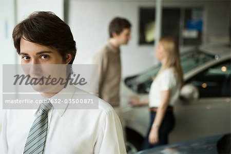 Car salesman in dealership showroom, potential buyers in background