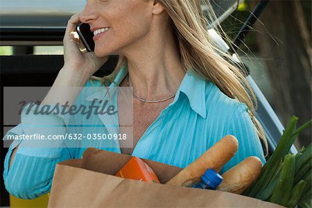 Woman using cell phone and holding bag of groceries