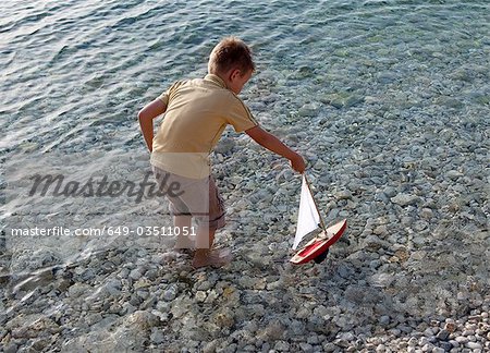 Garçon avec bateau de jouet à la plage