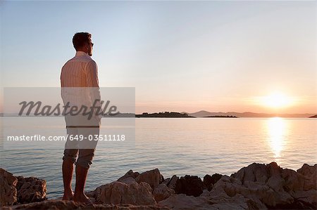 Man watching sun set at rocky beach