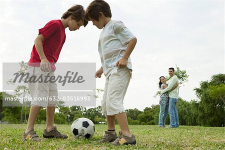Boys playing soccer, parents embracing in background