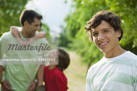 Teenage boy outdoors with father and younger brothers, portrait