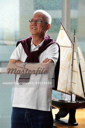 mature man folding his arms and smiling in front of model sail boat
