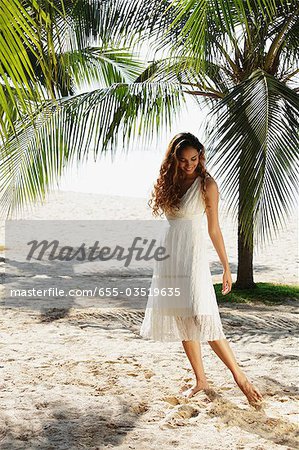 jeune femme qui marche dans le sable avec cocotiers en arrière-plan