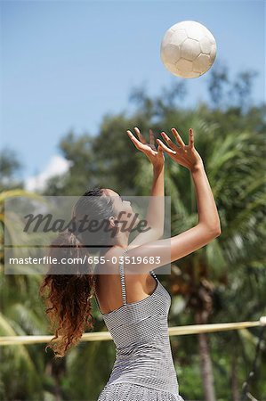 Junge Frau spielen Volleyball am Strand mit Kokospalmen als Hintergrund