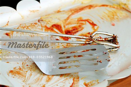 Pinces à barbecue et spatule sur plaque après une grillade Pinces à barbecue et spatule sur plaque après une grillade