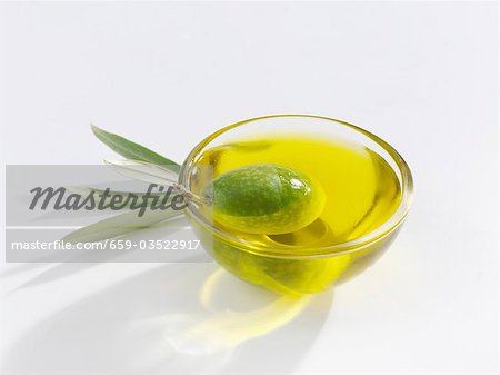 A green olive in a small glass dish of olive oil