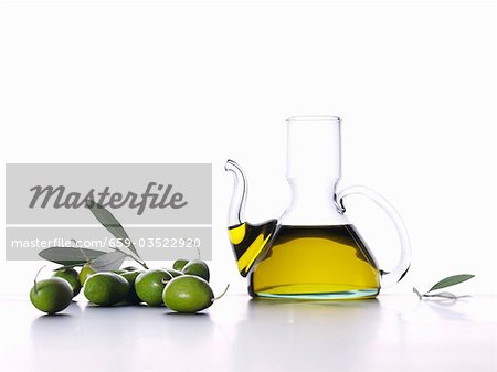 Olive oil in carafe, green olives and olive leaves